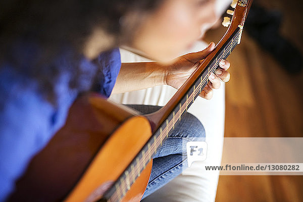High angle view woman playing guitar while sitting on sofa