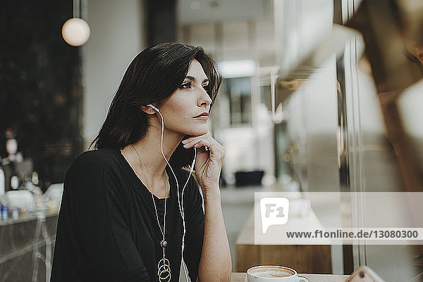Nachdenkliche Frau  die Musik hört  während sie durch das Fenster eines Cafés schaut