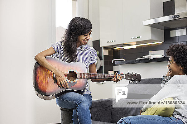 Woman playing guitar while resting with friend at home