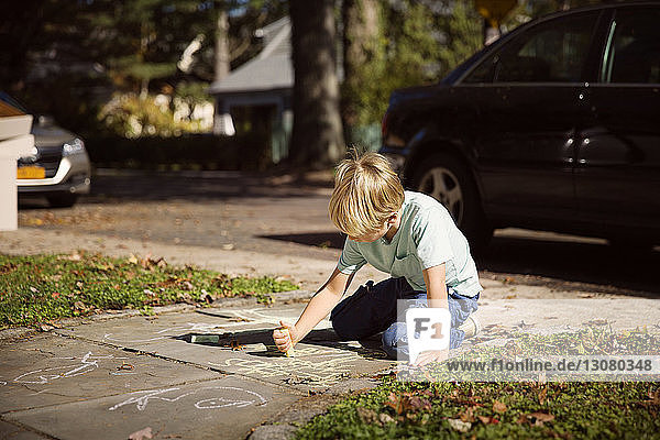Junge zeichnet mit Kreide  während er auf dem Fußweg kniet