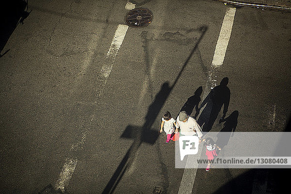 Hochwinkelansicht eines Großvaters  der die Hände der Enkelinnen beim Gehen auf der Straße hält