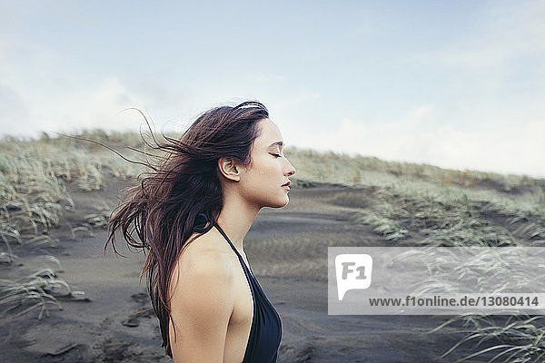 Seitenansicht einer Frau  die am Bethells Beach eine Brise gegen den Himmel genießt