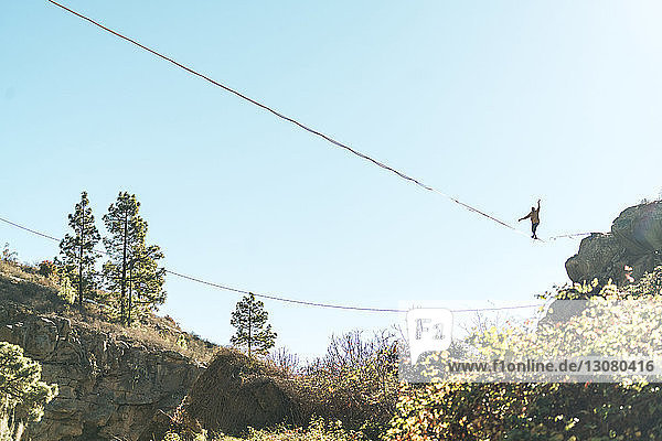 Low angle view of man slacklining against clear sky during sunny day
