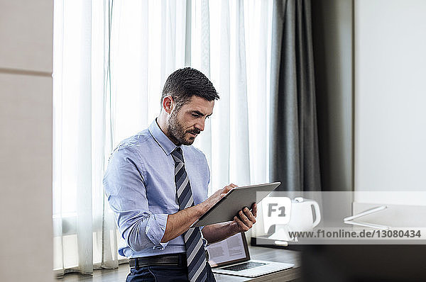 Geschäftsmann benutzt Tablet-Computer  während er am Fenster im Hotelzimmer steht