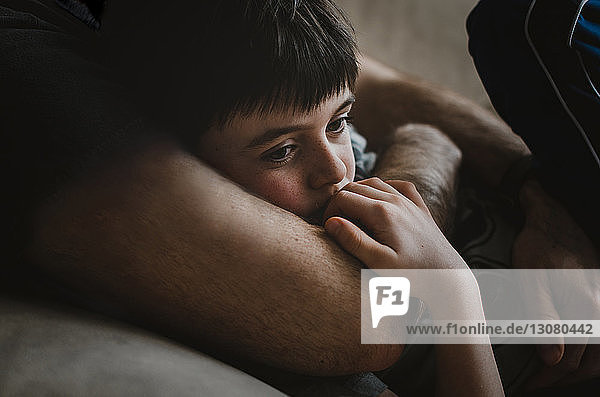 Mittelteil eines Vaters  der seinen nachdenklichen Sohn umarmt  während er zu Hause auf dem Sofa liegt