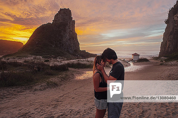 Seitenansicht eines romantischen Paares  das bei Sonnenuntergang am Strand steht