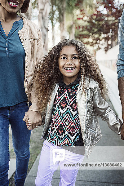Porträt eines glücklichen Mädchens  das mit seinen Eltern auf dem Bürgersteig geht