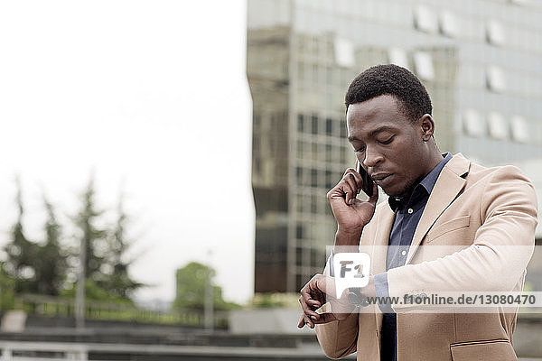 Geschäftsmann  der die Uhrzeit überprüft  während er ein Smartphone in der Stadt benutzt