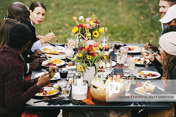 Friends eating food while sitting at dining table in backyard