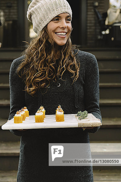 Happy woman holding appetizer on board while standing on steps