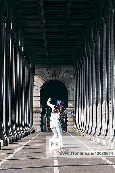 Rückansicht der Skateboard fahrenden Frau unter der Brücke in voller Länge