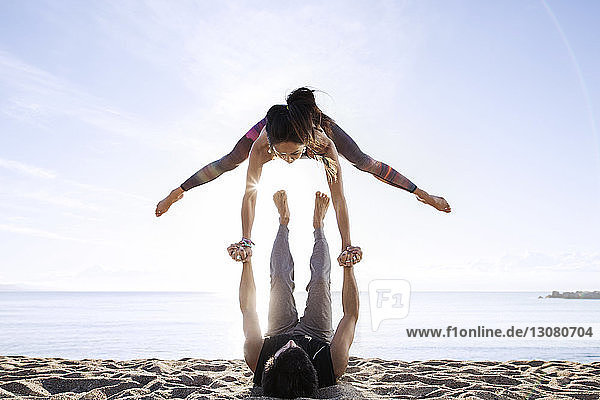 Mann hebt Frau beim Yoga am Strand im Sommer