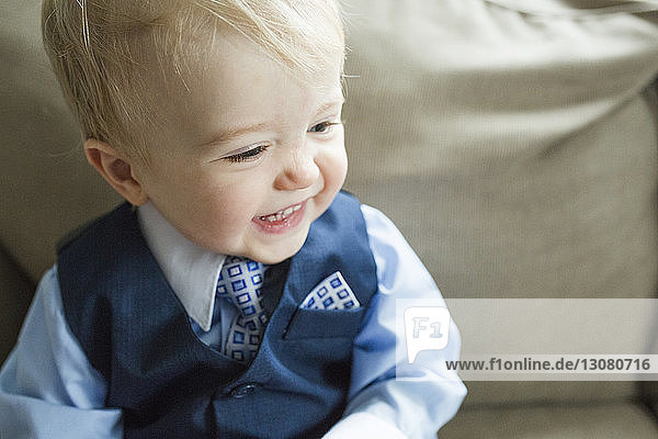 Nahaufnahme eines lächelnden süßen Babyjungen im Anzug  der zu Ostern zu Hause auf dem Sofa sitzt