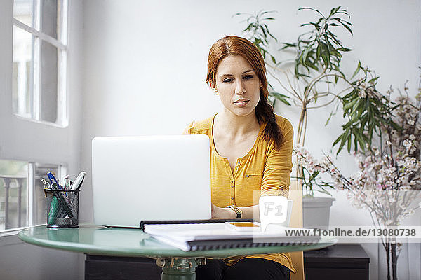 Nachdenkliche Geschäftsfrau arbeitet am Laptop am Tisch im Büro