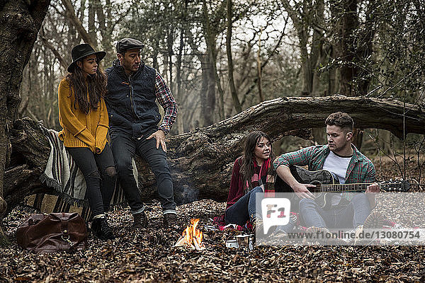 Man playing guitar while sitting with friends in Epping Forest