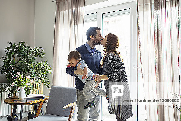 Mann  der einen Sohn trägt  während er zu Hause seine Frau am Fenster küsst