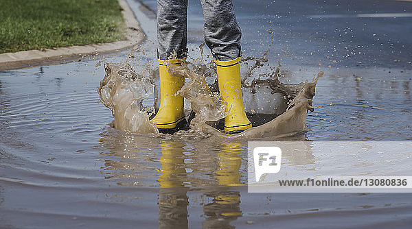 Low section of playful boy wearing yellow rubber boots while jumping in puddle