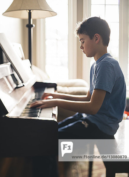 Side view of boy playing piano while sitting at home