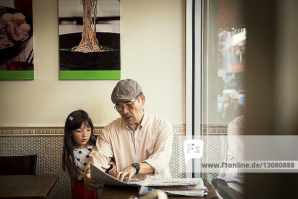 Grossvater zeigt Zeitung  während er mit seiner Enkelin im Restaurant sitzt