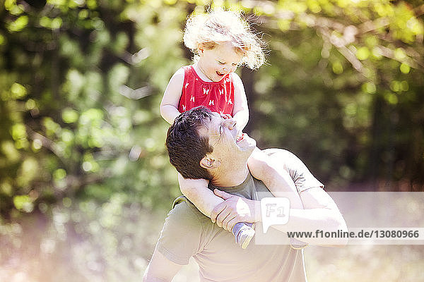 Glücklicher Vater trägt Tochter auf den Schultern im Park