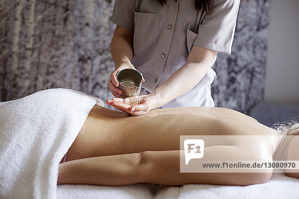 Midsection of female therapist pouring essential oil on woman's back in spa