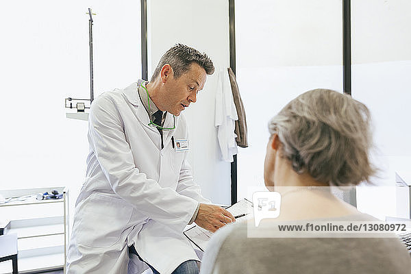 Arzt und ältere Frau schauen auf das Klemmbrett  während sie in einer medizinischen Klinik sitzen