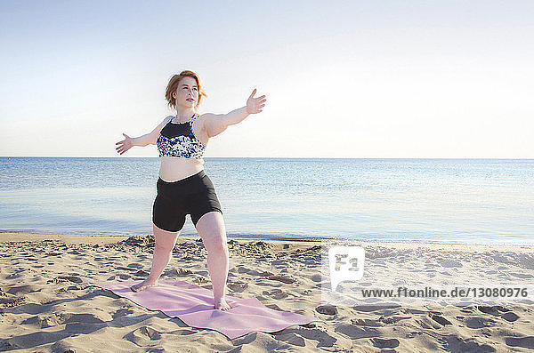 Frau übt Yoga-Pose am Strand bei klarem Himmel
