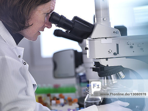 Seitenansicht einer Wissenschaftlerin  die im Labor Blutproben unter dem Mikroskop analysiert