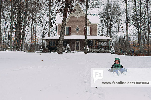 Boy lying on snow covered field against house