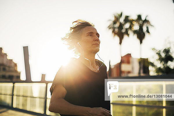 Nachdenkliche Frau schaut weg  während sie bei Sonnenuntergang an der Brücke Musik hört