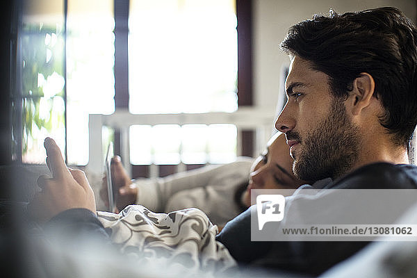 Nahaufnahme eines Paares  das zu Hause im Bett liegt und ein Smartphone benutzt