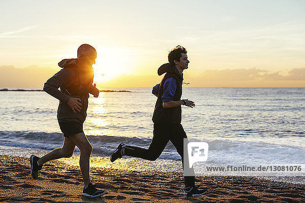 Vater und Sohn joggen bei Sonnenuntergang am Strand gegen das Meer