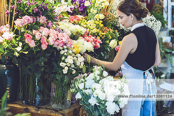Rear view of female florist picking roses from potted plants