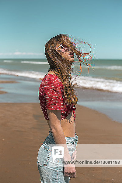 Side view of woman standing at beach against blue sky during sunny day