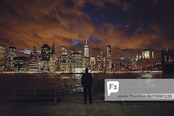 Rear view of man looking at illuminated skyline during night