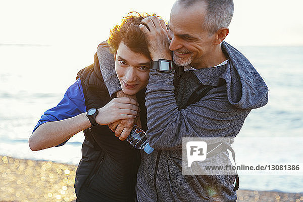 Portrait of happy son with playful father holding head at beach