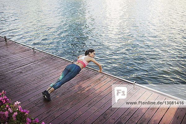 High angle view of woman performing pushups at wooden walkway by river