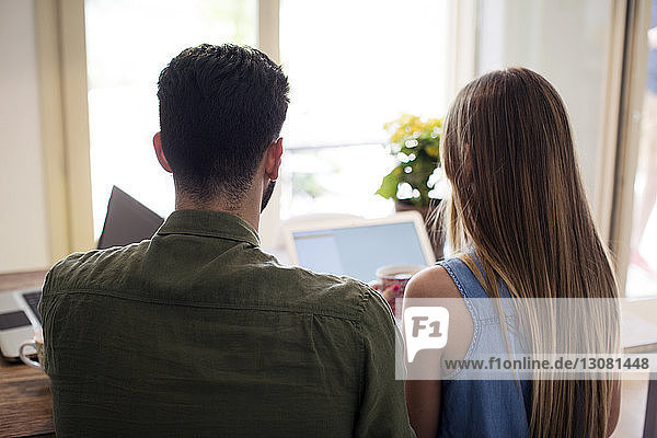 Rear view of couple using laptop at home