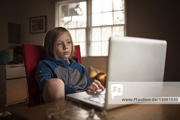Junge benutzt Laptop  während er am Tisch sitzt