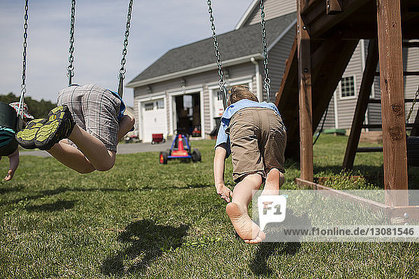 Brothers swinging in backyard during sunny day