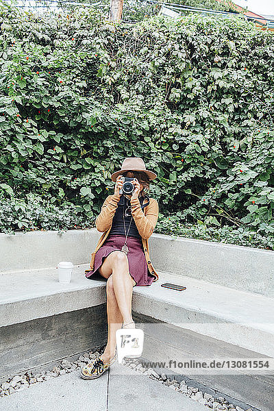 Frau in voller Länge beim Fotografieren auf einer Parkbank sitzend
