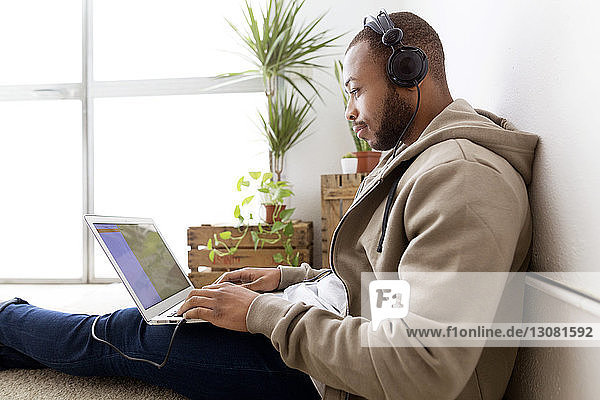 Side view of creative businessman listening music while using laptop in office