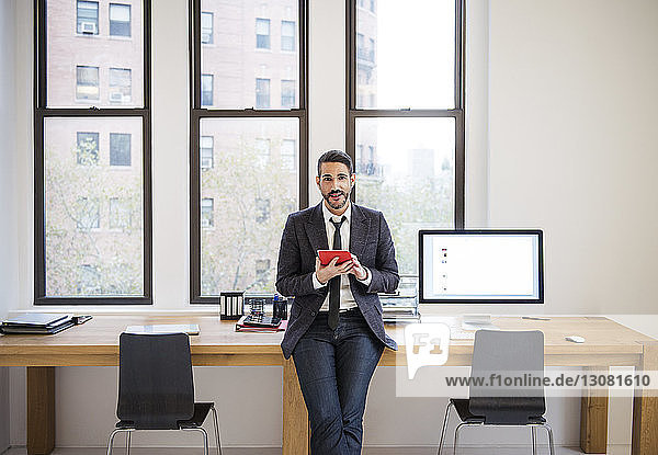 Portrait of businessman using tablet computer while leaning on desk in office