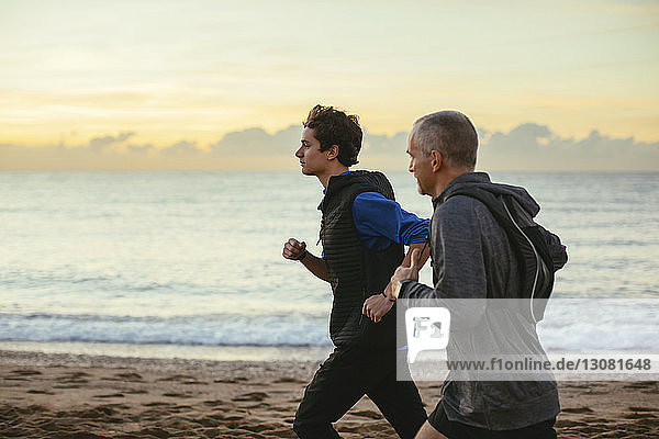 Vater und Sohn joggen bei Sonnenuntergang am Strand vor bewölktem Himmel