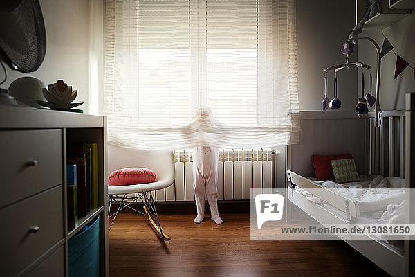 Girl hiding behind curtain at home