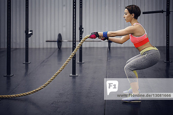 Seitenansicht einer selbstbewussten Sportlerin  die im Fitnessstudio mit Seil trainiert