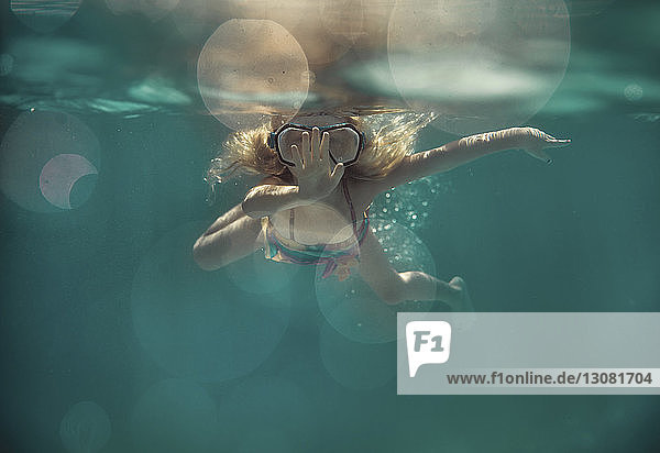Carefree girl wearing goggles while swimming underwater in pool