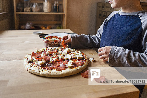 Midsection of boy preparing pizza at home