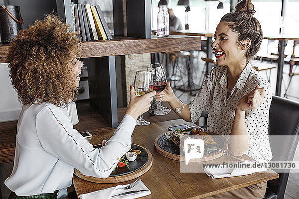 Happy businesswomen toasting wineglasses at table in restaurant