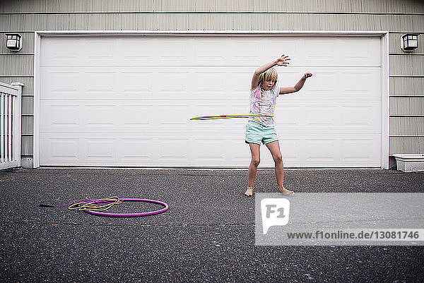 Mädchen spielt mit Kunststoffreifen  während sie auf der Straße gegen die Garage steht